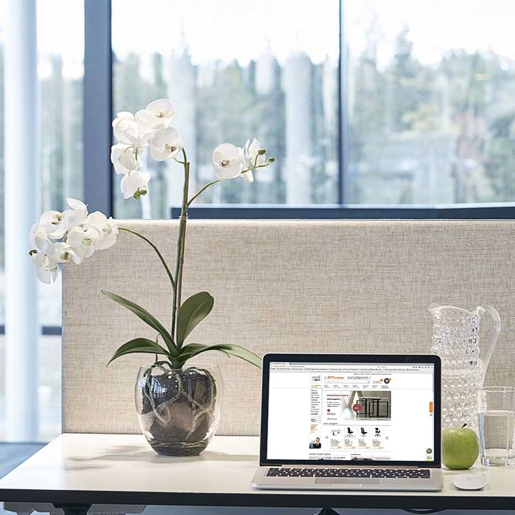 Kunstpflanze Orchidee Weiße Orchidee mit silbernem Topf. Kunstpflanze steht auf einem Schreibtisch neben einem Laptop. Dahinter eine graue Tischtrennwand.
