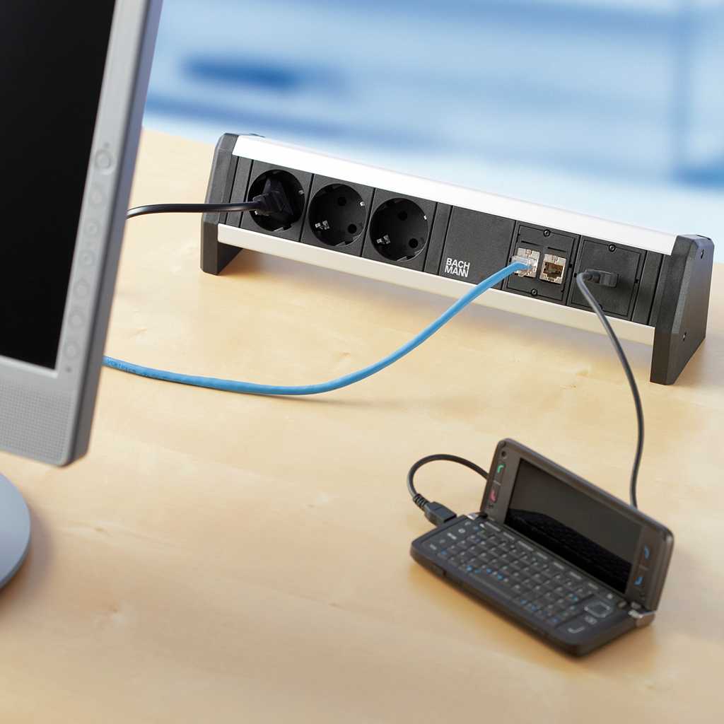 Steckdosenleiste für den Arbeitsplatz Media Box für den Tisch. MIt Steckdosen, USB Anschlüssen und HDMI Anschlüssen. An der Media Box lädt ein Handy auf. Ein Bildschirm ist angeschlossen.