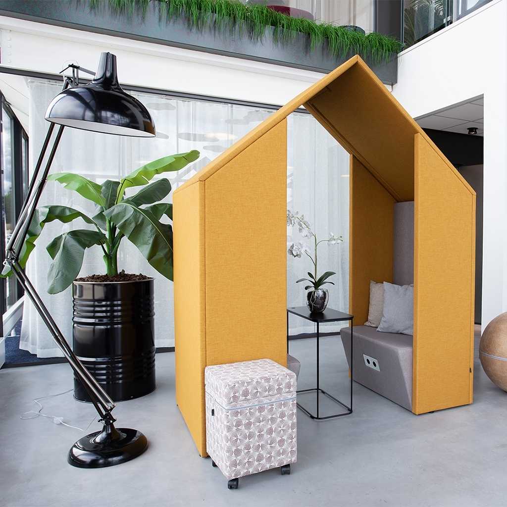 Openspace Möbel für Großraumbüro Gesprächsraum im Stil einer Hütte. Ausgestattet mit Sitzbank und Tisch. Hütte mit gelben Stoff bezogen. Hinten links eine große Pflanze, davor eine große Bürostehleuchte.