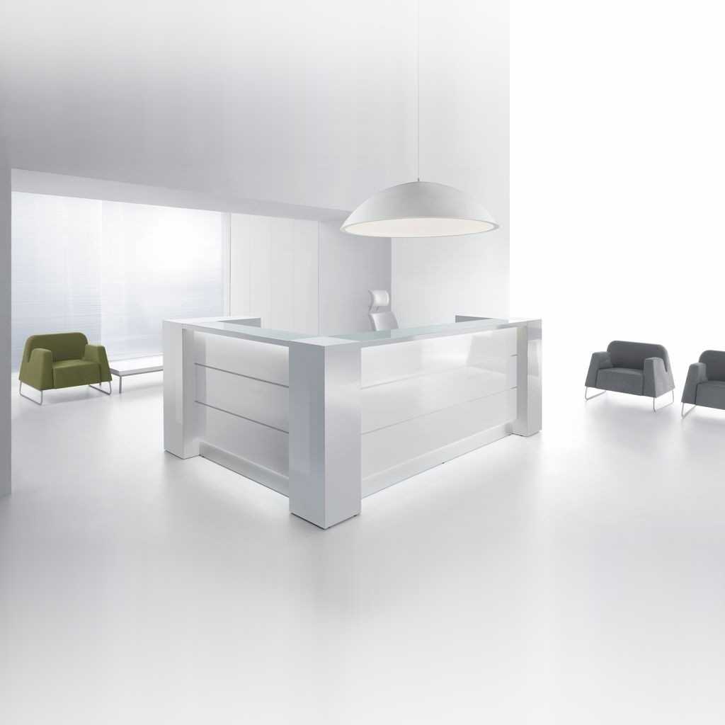 Weißer Empfangstresen mit Glaselementen Weiße Theke in L-Form mit Fronten und Platte aus Glas. Mit integrierter LED Beleuchtung und Zierelementen für eine moderne und klare Optik. Hiner der Theke ein weißer Drehstuhl. An den Seiten Lounge Sessel und ein kleiner Tisch. Über der Theke eine große, weiße Leuchte.