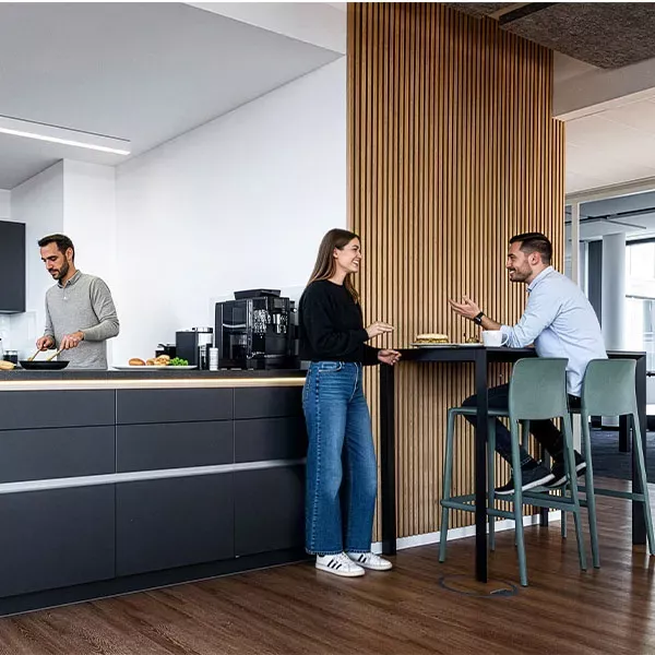 Büroküche mit Stehtisch und Barhockern vor Holzlamellenwand
