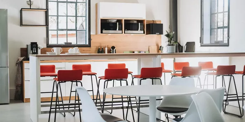Büroküche mit langer weißer Theke und Barhocker in Rot