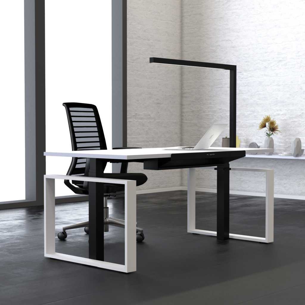 höhenverstellbarer Arbeitstisch fürs moderne Büro Bürotisch mit elektrischer Höhenverstellung. Weiße Platte mit schwarz-weißen Standfüßen. Am Büro-Arbeitstisch eine schwarze Arbeitslampe. Dahinter ein schwarzer Drehstuhl. Im Hintergrund ein bodentiefes Fenster.