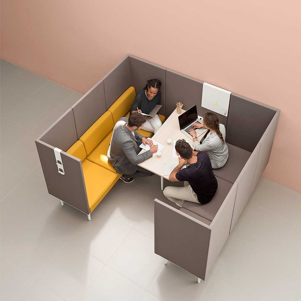 Möbelgruppe für Meetingpoint Blick von oben auf eine Sitzgruppe aus zwei Sofas. Links gelborange, rechts taupe; umrandet von einem taupefarbigen Sicht- und Akustikschutz. Um den Tisch in der Mitte sitzen vier Personen, eine mit Laptop.