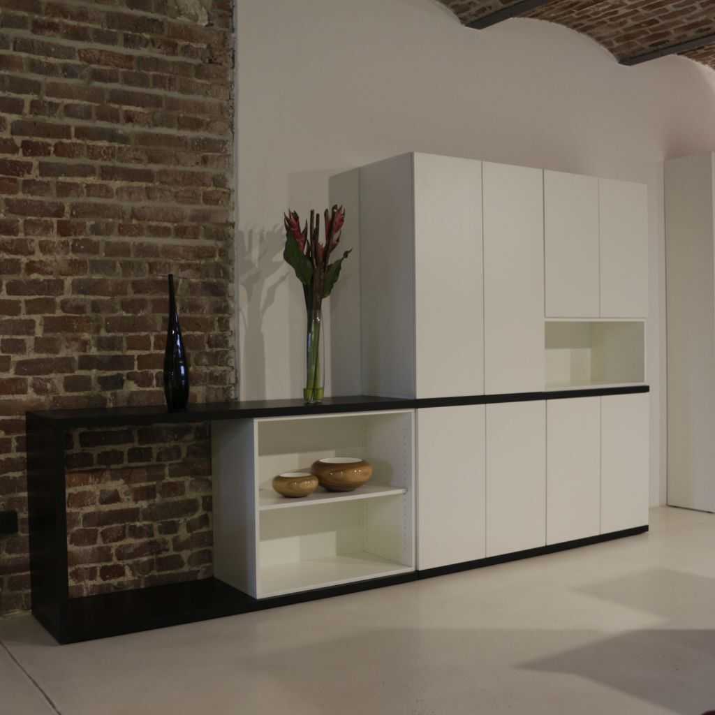 Schrankwand Büro Inwerk Paterio 5OH moderne Schrankwand im Büro. Weiße Fronten, rechts hohe Schränke mit Flügeltüren und mittig eine Duchreiche. Links ein offenes halbhohes Regal und ein halbhoher Schubladenschrank. Eingefasst von einer schwarzen durchgehenden schmalen Blende.