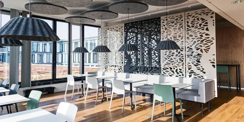 Lichtdurchflutete Cafeteria mit Akustiklampenschirmen und heller Einrichtung.