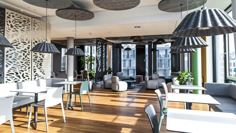 PROSTEP Group – Lichtdurchflutete Cafeteria mit hellen Möbeln und Akustikelementen an der Decke sowie akustisch wirksamen Deckenleuchten