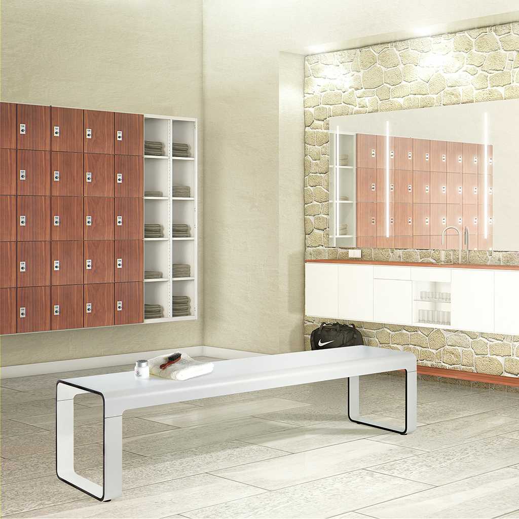 moderen Garderobenbank Heller moderner Umkleidraum. Links ein Fächerschrank mit abschließbaren Türen in Holzdekor und zwei Reihen offener Ablagefächer. Rechts ein Sideboard mit Waschplatz. Darüber eine großer Spiegel, mitten im Raum eine lange weiße Umkleidebank