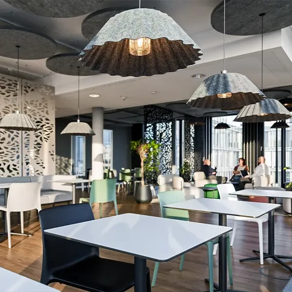 Cafeteria mit Tischen in weiß und Stühlen in Weiß, Grün und Blau sowei Leuchten mit Filzlampenschirmen