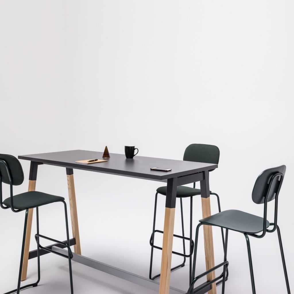 hoher Stehtisch mit schwarzer Platte und Holzbeinen. Um den Tisch drei schwarze hohe Stühle.