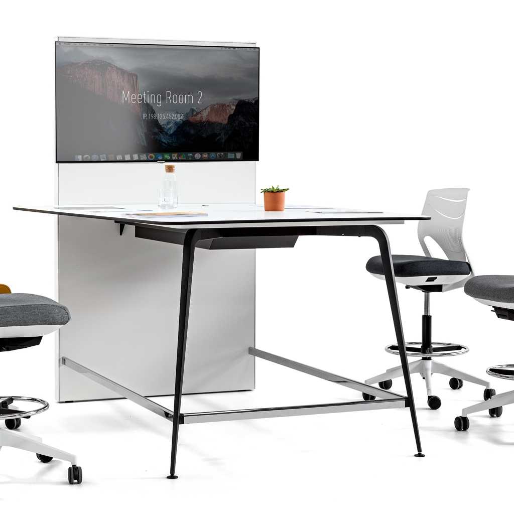 Kleiner Konferneztisch. Weiße Platte mit schwarzem Metallgestell. An der Stirnseite eine Displaywand mit Monitor. Um den hohen Tisch stehen drei Counterdrehstühle mit Rollen in weiß mit schwarzem Sitzpolster.