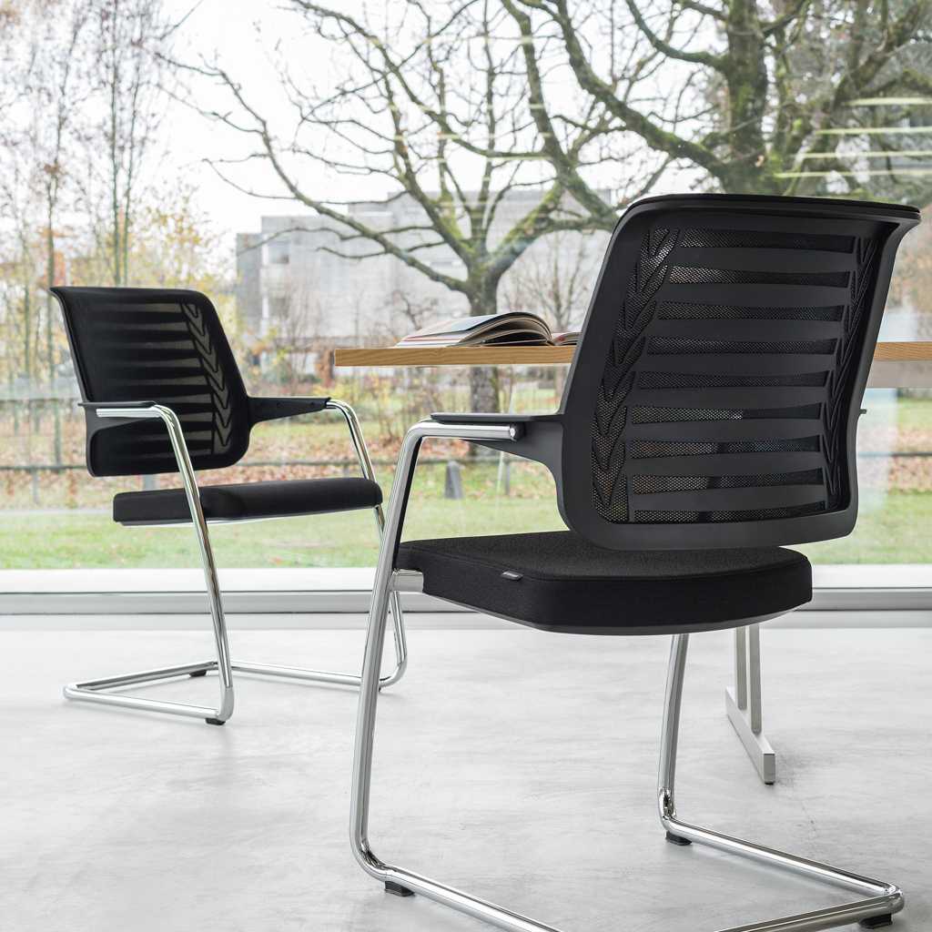 Freischwingerstühle klassische Schwingstühle in schwarz mit Metallgestell an einem Tisch mit Holzplatte.