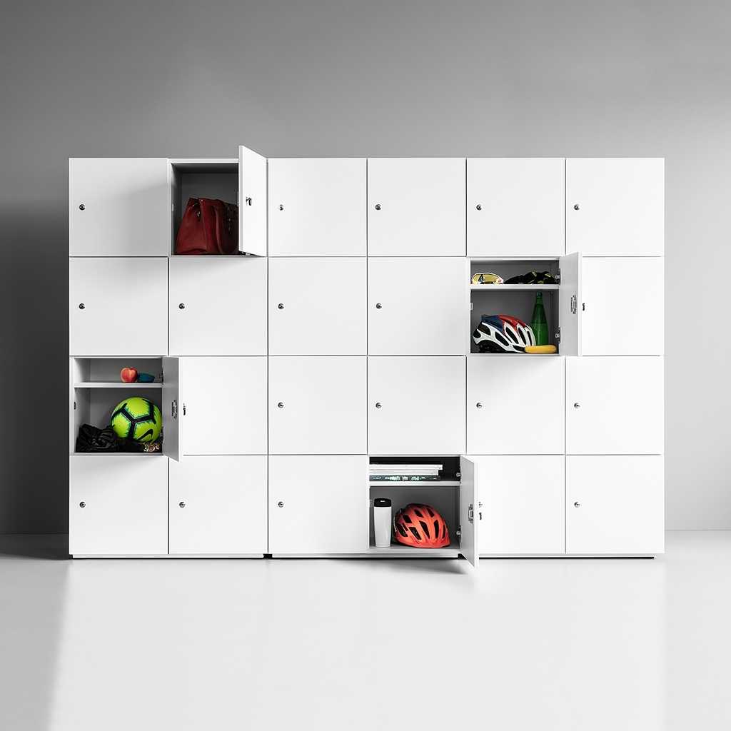 Schließfachschrank Wand mit einem Schrank mit Schließfächern. Die Fronten der Türen sind weiss. Es befinden sich vier Reihen mit jeweils fünf Fächern in dem Schrank. Die Türen vor den Fächern sind abschließbar. In jeder Reihe ist eine Tür geöffnet und bietet einen Blick auf den aufbewahrten Inhalt wie Taschen, Sportutensilien und Helme.