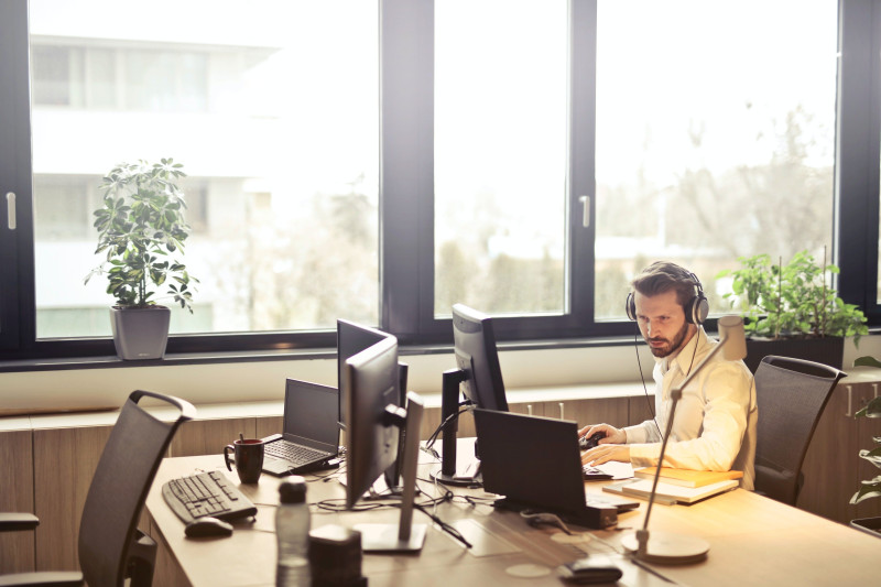 Büromitarbeiter sitzt vor dem Computer und trägt Noise-Cancelling-Kopfhörer