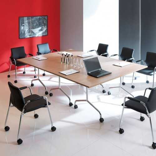 Klapptisch für Meeting Klapptische in einem Meetingraum zu einer großen Tischfläche zusammengestellt. Vorne steht ein aufgeplatter Lapptop auf dem Tisch. Hinten, an einer roten Wand hängt ein Monitor. Um die Tischfläche verteilt stehen schs schwarze Stühle. Im Hintergrund ist ein großese Fenster zum Teil von einer Lichtschutzgardine verdeckt.