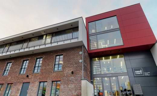 Bildausschnitt zeigt den Eingangsbereich des Forums für Bürokultur, Links original Ziegelmauerwerk, rechts moderne schwarz rote Fassade